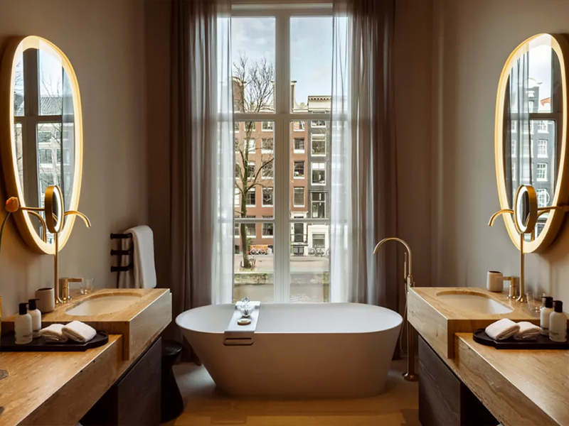 The bathroom seamlessly blends modern and minimalist design, where the self-care journey starts with a Dyson supersonic hair dryer, votary bath care, and a standalone tub that promises perched-high canal views. Image Credit: Rosewood Amsterdam)