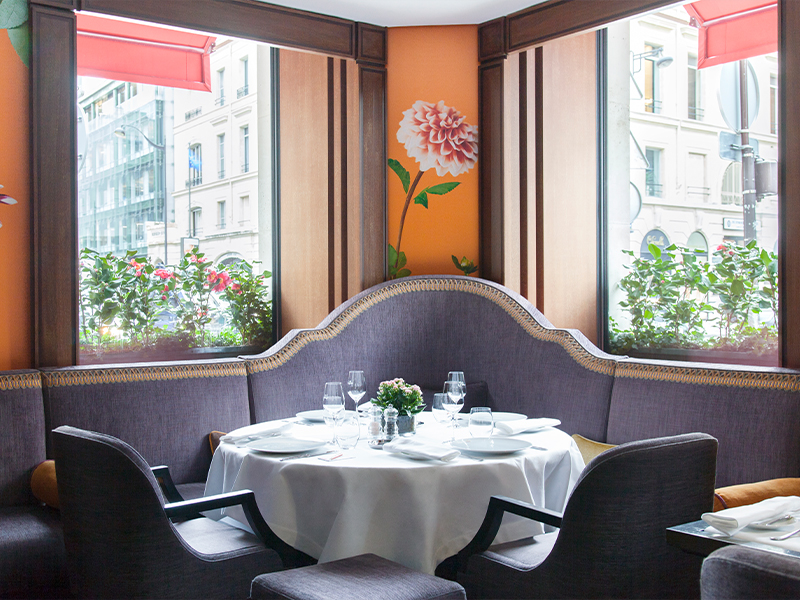 114 Faubourg is a vibrant brasserie where bold pops of colour like orange floral wallpaper, rich purple sofas, and an ornate wrought-iron staircase come together to create a warm, elegant atmosphere with unmistakable Parisian flair. ( Image Credit: Le Bristol Paris) 
