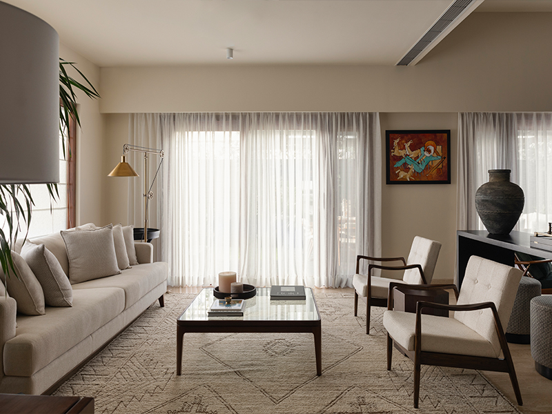 In the light-soaked living room, a beige rug from Jaipur Rugs holds a sofa and glass centre table from Tianu and refurbished vintage armchairs. (Image Credits: Phosart Studio)