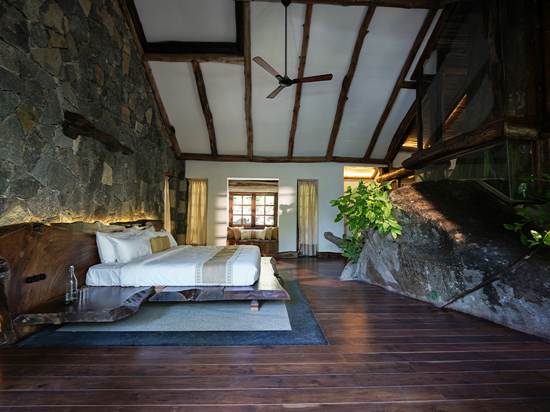 A standout feature is the master bedroom, where an in-situ rock formation grounds the space in its earthy surroundings. (Image Credits: Earthitects) 