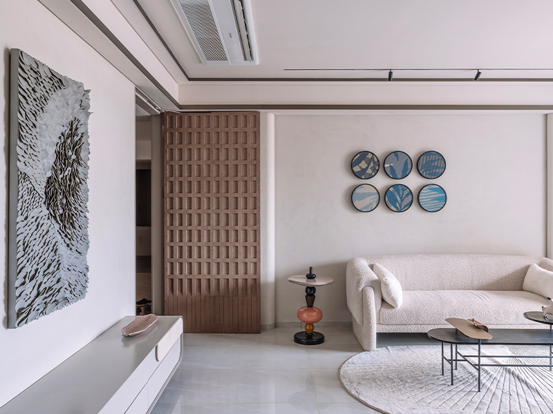 At Caramel House by Verizon Architects, the boucle Pulezzi sofa is paired with a rug from Oneglobe Exim that adds a touch of softness. Wooden panels, artwork by Sachi Prajapati above the console, and artefacts from the Ratios Store exude a layered effect. (Image Credits: Inclined Studio)
