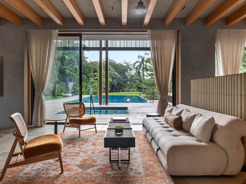 Overlooking the pool and the landscape beyond, this living room has furniture by DTale Modern, soft furnishings by Bonnie & Saks, and carpet from Obeetee for a bit of colour. (Image Credits: PHX India) 