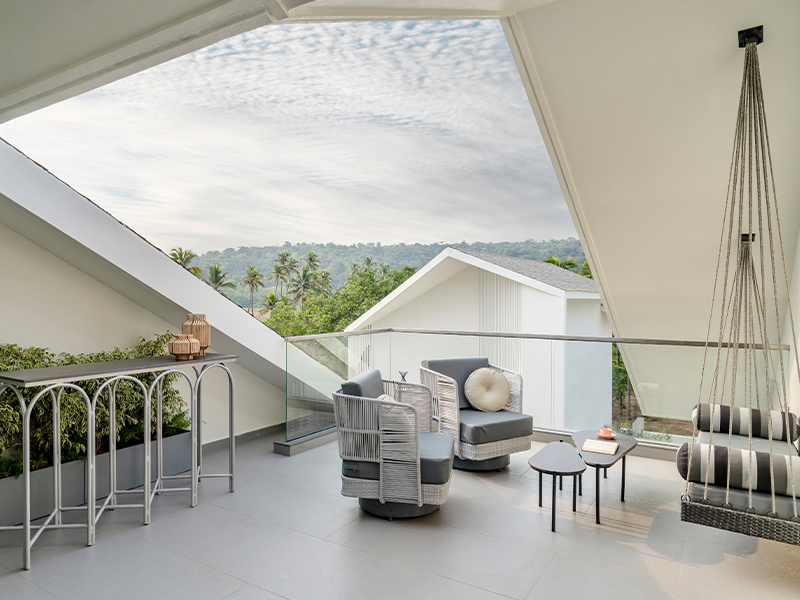 The sit-out in the attic looks out at the sweeping views of the paddy fields and towering trees featuring bespoke armchairs and coffee tables paired with a swing, perfect for watching the sunset. (Image Credits: Yadnyesh Joshi and Nikhil Paliwal)
