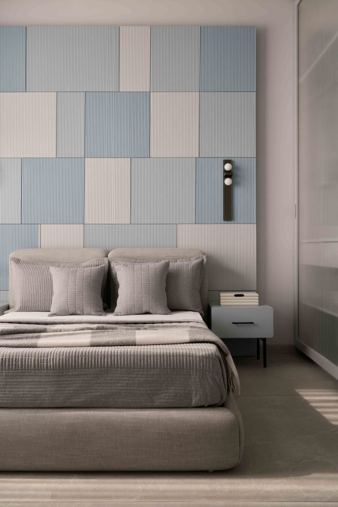 In the master bedroom, the tactile fluted wall panelling in shades of blue is finished with ICA paints. The bed and side table are designed by NH48, and the upholstered bedding material is from Housewarming. Locally picked wall sconces lend an ambient glow after sundown. 
(Image Credits: Yadnyesh Joshi)
