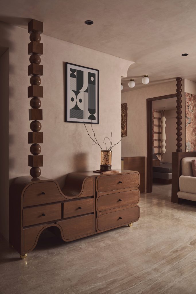 In the entryway, a custom console with undulating volumes plays with symmetry and shadow, forging a dialogue with geometric totems and graphic art. Lime-wash textured paint from SurfaceX envelops the walls. (Image Credits: Yadnyesh Joshi)
