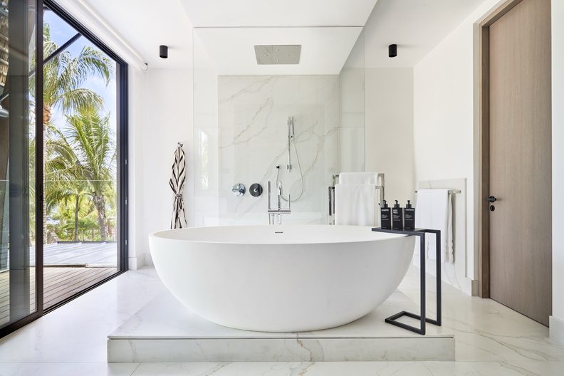 This stylish island energy extends to the bathrooms, where guests can indulge in the waterfall spray of the KOHLER® Loure™ rain panel or unwind in a freestanding bathtub, complete with matte black faucets and shower trim that tie the aesthetic together. (Image Credit: Tom Fallon) 
