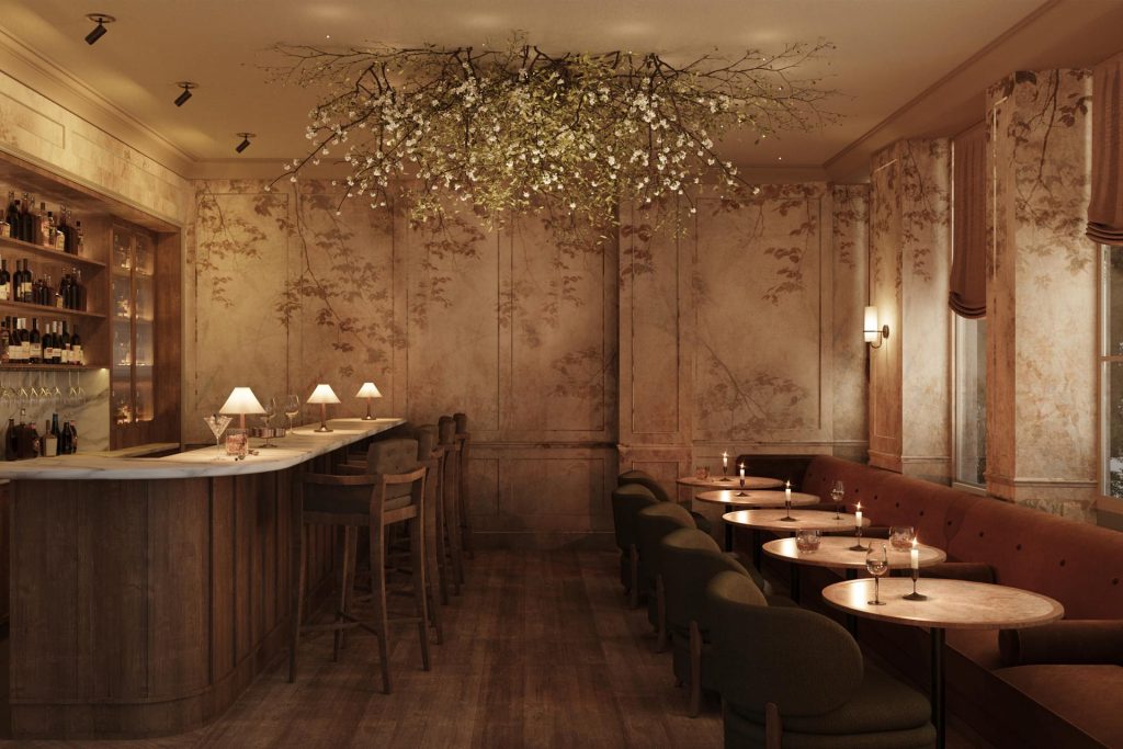 British artist Tess Newall has painted softly layered silhouettes of branches onto a textured limewash background at the bar, using an earthy colour palette that harmonises beautifully with Cox London’s oak branch chandelier. Image Credit: (Templeton Gardens-Miiro Hotels) 
