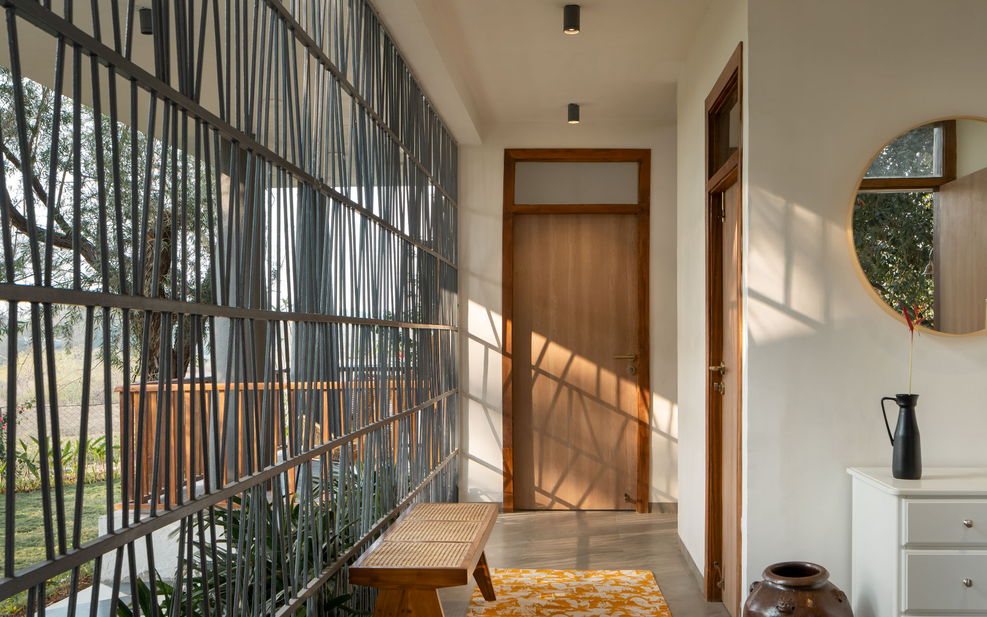 The mullioned screen along the breezeway orchestrates an interplay of light and shadow on the wood wicker bench from Freedom Tree and the rug from Saphed Home, while the vases are from Ware Innovations. (Image Credits: Ekansh Goel)