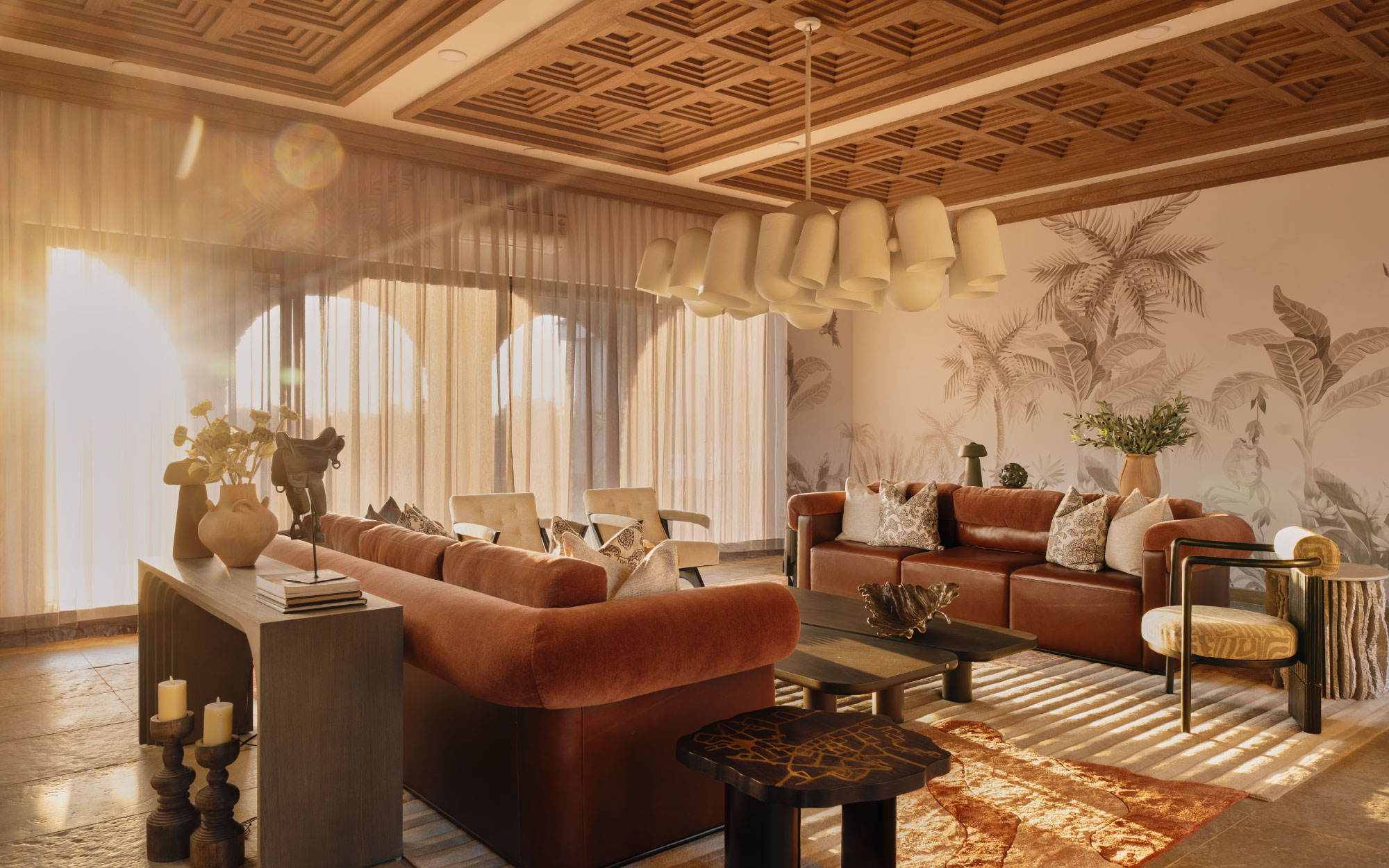 The living room commands attention with a dramatic cluster of Guccha light—lingam-inspired forms suspended mid-air by Ashiesh Shah Studio. Tropical palms and beach-inspired wallpaper by Artisan Furnishings tie the entire space together with a sense of laid-back elegance. (Image Credits: Rohit Mendiratta)