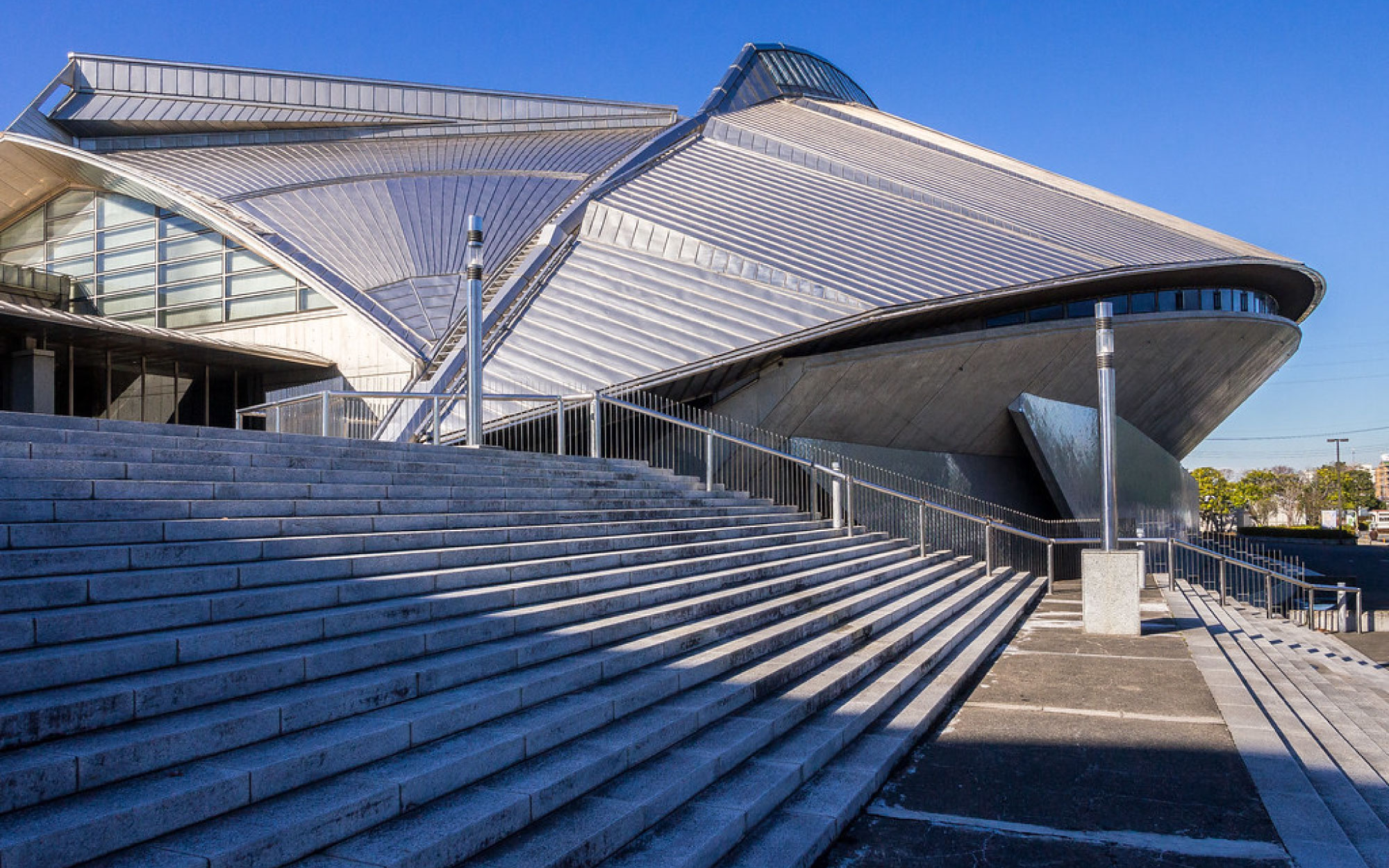 At the Fujisawa Municipal Gymnasium, Fumihiko Maki wraps two arenas beneath a hovering stainless-steel roof, creating a structure that shifts subtly with light and movement. (Image Credits: Jacome from Flickr) 